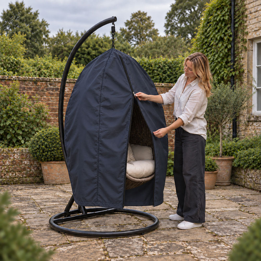 A woman unzipping a navy custom egg chair cover fitted to the pod of a hanging egg chair on a stone garden patio