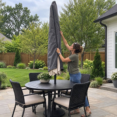 A woman fitting a made-to-measure charcoal parasol cover over a closed patio umbrella standing through a garden dining table